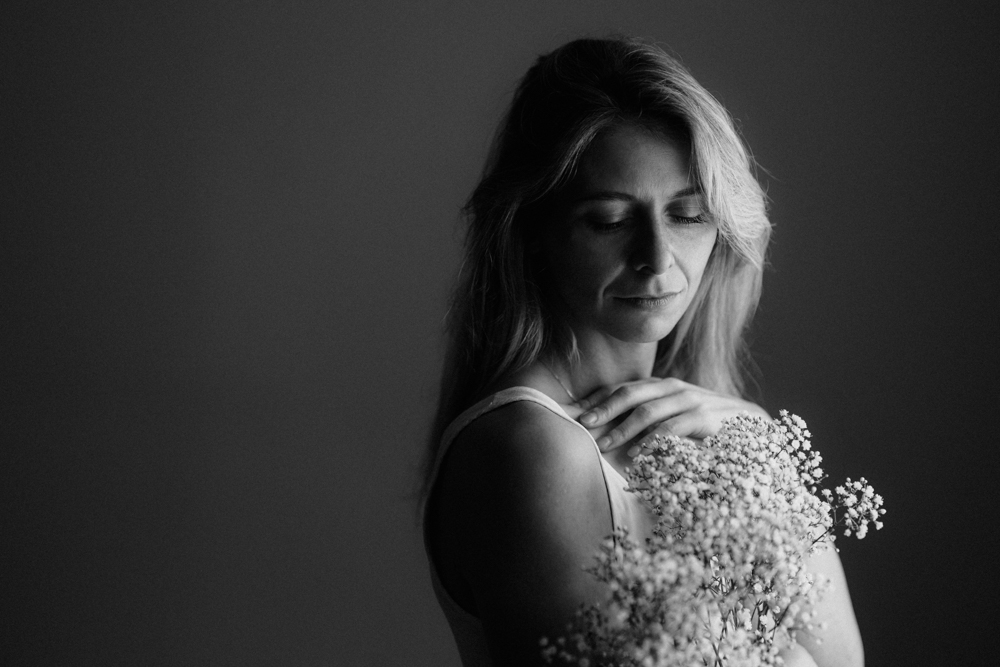 Schwarzweißbild einer Frau die sinnlich zur Seite schaut und einen staut weißer Blumen in der Hand hält