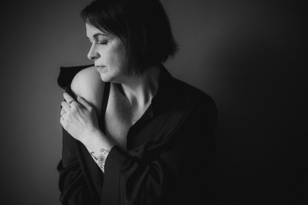 Frau schaut seitlich zum Licht und schiebt sich sinnlich die Bluse von ihrer Schulter